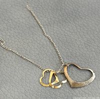 Close-up of necklace chain with three heart pendants showing contrasting metal colors and textures.
