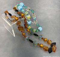 Both necklaces displayed together on a white stand showing variety in bead colors and shapes.