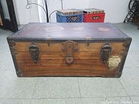 Front view of antique wooden trunk showing two locking clasps, central lock, and metal reinforced corners with visible patina and wear.