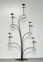 Full front view of the metal hat rack showing six upward branching arms with circular holders for hats, and flat square base for stability.