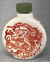 Front view of the white ceramic snuff bottle with red hand painted dragon design and green stopper