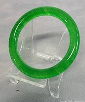Front view of the translucent green jade bangle displayed on a clear stand, showing the smooth, polished surface and the consistent green color.