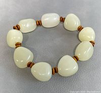 Full bracelet laid flat on surface showing all nine white jade beads separated by small brown spacer beads