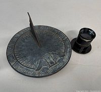 Cast iron sundial with raised eagle design and inscription seen with Ross London magnifier lens nearby.