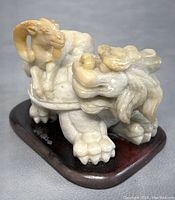 Side view of the white jade Foo Dog with a Ram on its shell back showcasing carving details and wooden base.