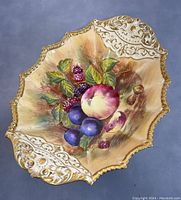 Top-down view showing the detailed hand-painted fruit and ornate gold decoration on the shell shaped footed bowl.