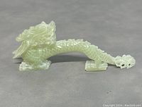 Side view of light green jade carved dragon showing detailed scales, head, and claws.
