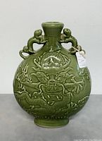 Front view of vintage Chinese green ceramic vase with raised dragon design and sculpted handles.