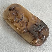 Top angle view showing hand carved designs and color gradient on natural jade pendant.