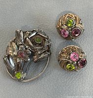 Front view of the sterling silver Hobe brooch and matching round crystal earrings placed on a light grey surface.