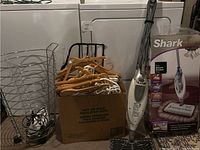Laundry basket, box of hangers, Shark mop with box, and iron grouped together showing full lot contents.