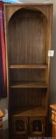 Photo of tall wooden book shelf with three shelves and bottom cabinet.