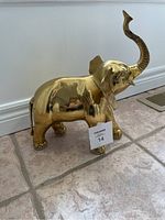 Side profile of the polished brass elephant statue showing the raised trunk, large ear, and golden finish.