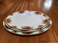 Three stacked Royal Albert Old Country Roses serving plates, staged on hardwood floor, showing floral pattern and gold trim.
