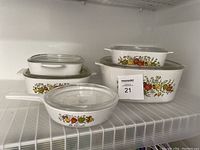 Overview photo showing 4 rectangular CorningWare casserole dishes stacked with lids and 1 round sauce pan with handle and lid, featuring Le Persil fruit and vegetable pattern
