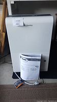 Front view of white Danby dehumidifier with owner's manual placed against it and visible power cord.