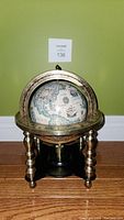 Front view of desktop globe showing the vintage map and metal frame with four turned legs and solid black base