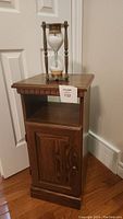 Wood end table with square top, open middle shelf, and cabinet at bottom. Medium dark wood with brass handle.