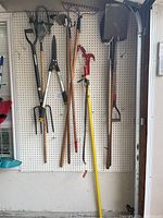 Image showing rakes, clippers, hoe, and other long-handled gardening tools hanging on pegboard.