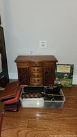 Front view of wooden jewelry box with wallets in plastic container and book behind it.