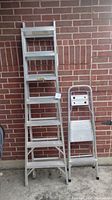 Both an aluminum multi-way combination ladder and a smaller aluminum step stool side by side against a brick wall.