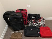 Multiple luggage including black and red wheeled suitcases, zebra print duffel bag, black carry-ons, and red handbag on carpeted floor