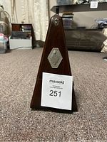 Front view of wooden pyramid-shaped metronome with metal plaque and lot number card attached.
