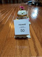 Side-angle view highlighting the hand crank mechanism and floral embellishments on top.