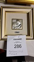 Full front view of the framed Madonna and Child silver art, showing the square frame with gold and cream tones and hanging latch on the back.
