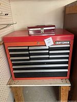 Red Craftsman toolbox with multiple drawers on a stand. Shows brand label and various sized drawers.