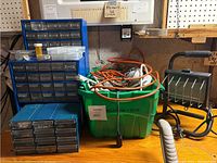 Photo of two small drawer cabinets, green tote with extension cords, and the work lamp on a wooden surface.