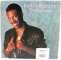 Front cover of Eddie Murphy: Comedian vinyl LP album showing Eddie Murphy in black leather jacket on marbled blue background.