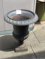 Full side view of the large black cast iron urn showing its shape, base, and rim detail, placed outdoors on stone paving