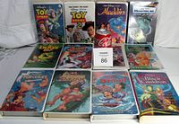 Photo showing 12 Disney VHS tapes featuring titles like Toy Story 1 and 2, Aladdin, Monsters Inc., A Bug's Life, The Emperor's New Groove, The Polar Express, Hercules, Tarzan, Lilo & Stitch, and The Black Cauldron in cases.