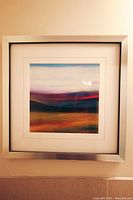 Full view of the abstract wall art hung on a beige wall, showing the silver frame and abstract colorful image.