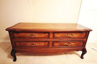 Front view of the antique wooden trunk showing ornate brass handles and curved legs.