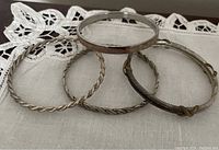 Photo of four bracelets displayed on a lace cloth background, showing different styles including twisted wire and solid bangle