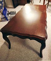 Photo of a dark polished wooden coffee table showing the top surface, scalloped edges, and curved cabriole legs.