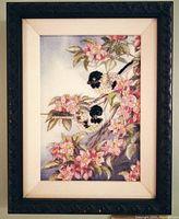 Framed cross stitched artwork showing two birds on a flowering branch.