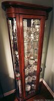 Front and angled side view of wooden corner curio cabinet showcasing glass door panel and shelves inside.