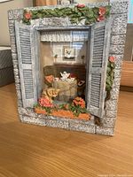 Front view of dimensional figurine depicting a cat at a breakfast window with stone frame, shutters, floral accents, and miniature table setting.