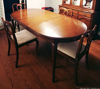 Photo showing the solid mahogany oval dining table with four matching chairs around it, highlighting the wood grain and shape.