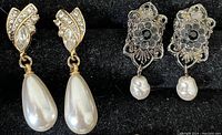 Photo of two sets of earrings, one gold-tone with rhinestones and teardrop pearl, the other silver-tone filigree with black stones and round pearl drops.