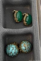 Two sets of clip-on earrings; one pair with green oval stones and gold-tone metal, another pair with round turquoise-colored crackled stones in gold-tone metal frames.