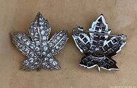 Front and back view of a leaf-shaped jewelry pin with clear rhinestones and silver-tone metal backing with pin clasp.