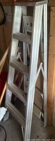 Photo showing aluminum foldable step ladder with four steps, side braces, and handles.