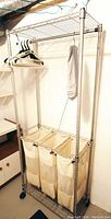 Photo of laundry sorter showing sturdy steel frame, three canvas sorter bags, top shelf, and hanging rod with hangers