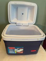 Photo of a rectangular Rubbermaid lunch cooler with an open white lid showing the interior. Blue exterior with a red Rubbermaid logo on the front.