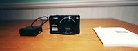 Image of the Nikon Coolpix digital camera, charger, and instruction manual on a wooden surface.