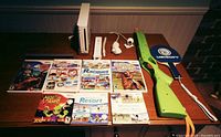Nintendo Wii console, controllers, game paddle, light gun, and 7 Wii games arranged on a wooden surface.